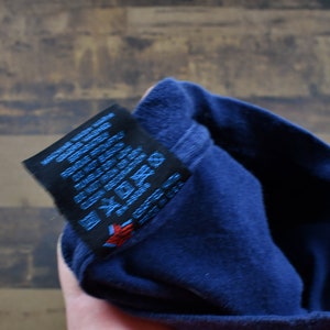 May include: Close-up of a navy blue t-shirt with a black care label. The label has text in English, French, German, Spanish, Italian, and Japanese. The label also has symbols for washing, drying, and ironing.