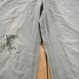 May include: A pair of light grey work trousers with a large hole in the left knee and smaller holes on the right leg.