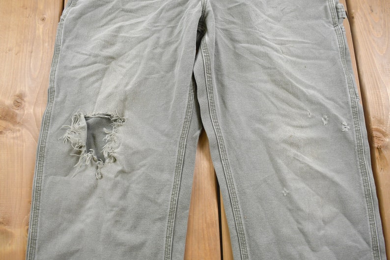 May include: A pair of light grey work trousers with a large hole in the left knee and smaller holes on the right leg.