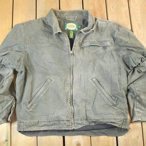 Puede incluir: Chaqueta verde oliva descolorida con cierre de cremallera completo, dos bolsillos delanteros y cuello. La chaqueta tiene una pequeña etiqueta en el cuello. La chaqueta está hecha de un material duradero.