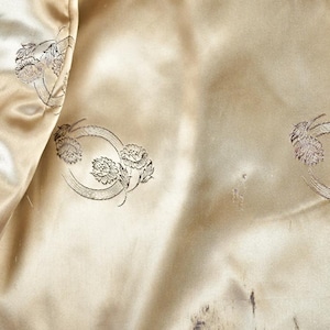 May include: Close-up of the interior lining of a vintage coat. The lining is a light beige satin with a subtle sheen. Decorative floral embroidery in a circular pattern is visible. The coat's fur trim is visible on the right side.