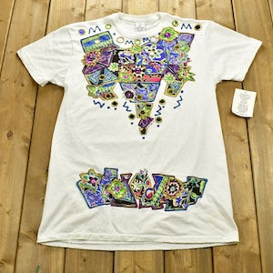 May include: White t-shirt with a colorful, geometric design featuring flowers and abstract shapes. The design is centered on the front of the shirt and includes the text "MOMO".