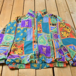 May include: A vintage zip-up jacket with a vibrant patchwork design. The jacket features a mix of teal, purple, red, and gold patterns, including paisley, floral, and geometric shapes. The jacket has a high collar and elastic cuffs and hem.