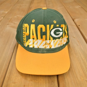 May include: Green Bay Packers baseball cap with a yellow brim and a green and white embroidered logo. The logo says "Packers" and "Green Bay Packers" on the side.