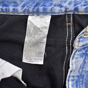May include: A close-up of a blue denim jean label with white stitching. The label has text that reads "8165 08T 34 X 32 Relaxed Fit".