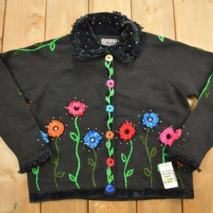 May include: Black cardigan sweater with a velvet collar and floral embroidery. The flowers are multi-colored and have green stems. The cardigan has a button closure.