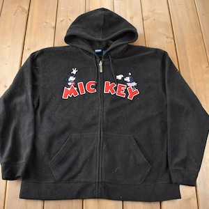 May include: Black fleece hoodie with a zipper closure and a Mickey Mouse graphic on the front. The graphic features Mickey Mouse and his friends in a line, with the word "Mickey" in red letters and the word "Key" in black letters.
