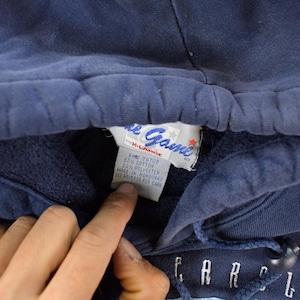 K&ouml;nnte beinhalten: Nahaufnahme eines marineblauen Kapuzenpullovers. Das Etikett lautet "The Game" und "X-Large". Der Pullover hat einen Kordelzug und das Wort "CAROLINA" ist in wei&szlig;en Buchstaben zu sehen.