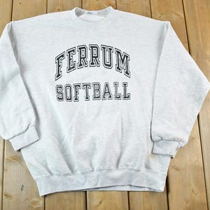 May include: A light gray sweatshirt with the words "FERRUM SOFTBALL" printed in black block letters. The sweatshirt has a crew neck, long sleeves, and ribbed cuffs and hem. The garment is made of a soft, comfortable material.