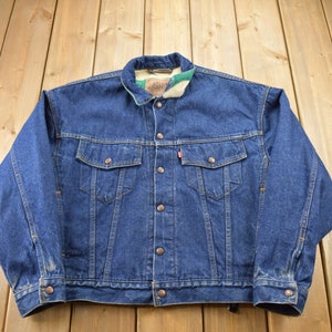May include: A blue denim jacket with a brown button closure and a plaid flannel lining. The jacket has two front pockets and a single pocket on the left chest.