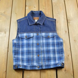 May include: A blue denim vest with a plaid pattern on the bottom half. The vest has a button closure and two pockets.
