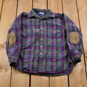 May include: A long-sleeved plaid flannel shirt with elbow patches. The shirt is purple, green, and blue with a white background.