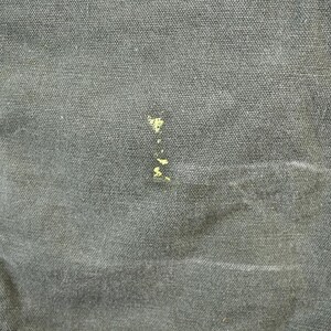 Pu&ograve; includere: Primo piano di un tessuto denim grigio con una piccola macchia gialla.