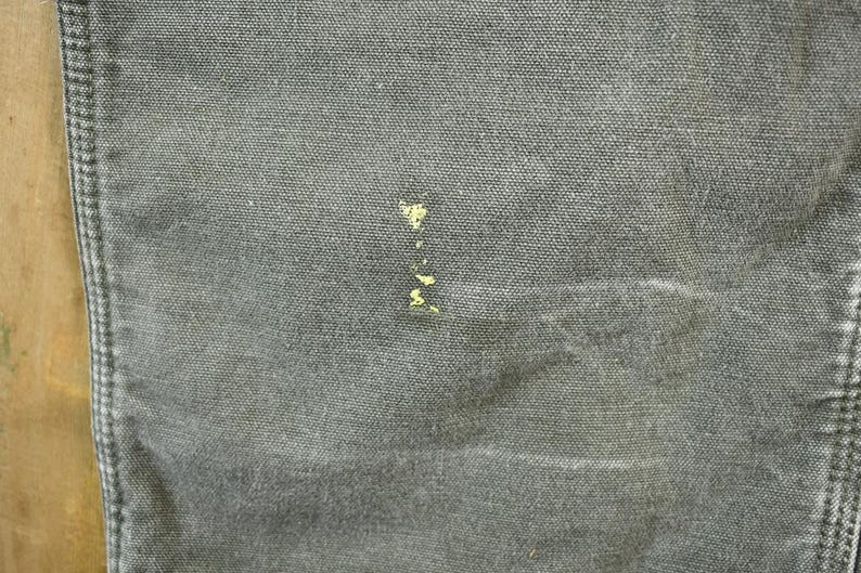 Pu&ograve; includere: Primo piano di un tessuto denim grigio con una piccola macchia gialla.