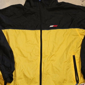 Pu&ograve; includere: Una giacca a vento gialla e nera con un bordo blu e un piccolo logo sul petto.