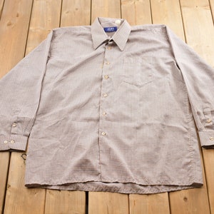 May include: A long-sleeved, button-down shirt with a checkered pattern in shades of brown and white. The shirt has a blue label with the word "ALPS" on the collar.