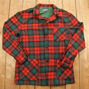 May include: A red and green plaid flannel shirt with a button-up front and two large pockets.