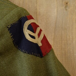 May include: A green military jacket with a red, white, and blue patch sewn on the sleeve. The patch features a stylized symbol.
