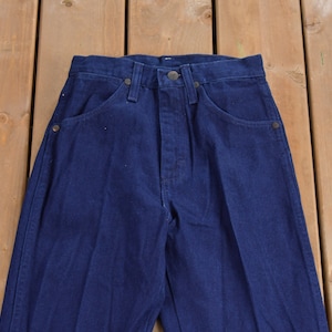 May include: A pair of dark blue denim jeans with a straight leg fit. The jeans have a classic five-pocket style and a button fly.
