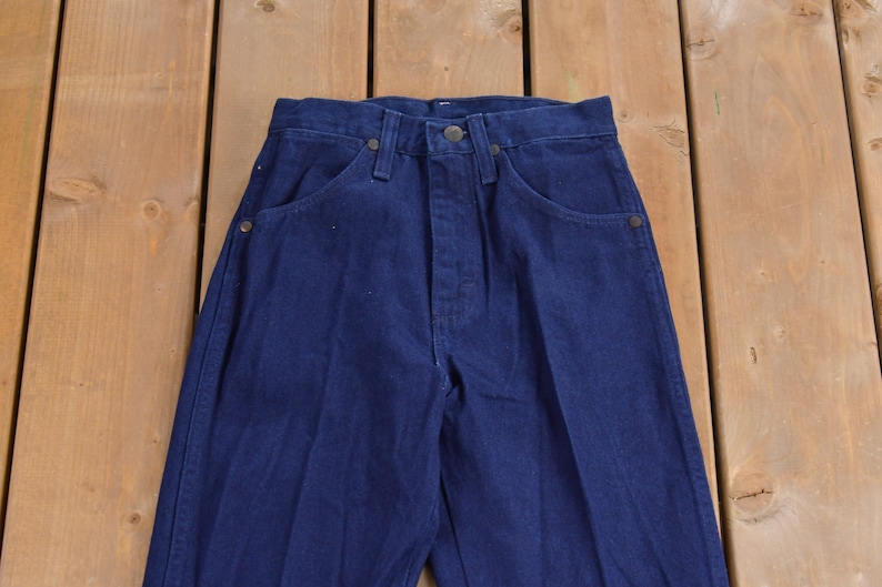 May include: A pair of dark blue denim jeans with a straight leg fit. The jeans have a classic five-pocket style and a button fly.