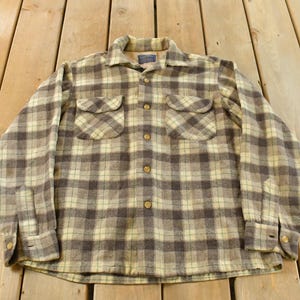 May include: A brown, cream, and tan plaid shirt with long sleeves and a button-down front. The shirt features two chest pockets and a collared neckline. The fabric is a soft, woven material, ideal for autumn or winter wear.