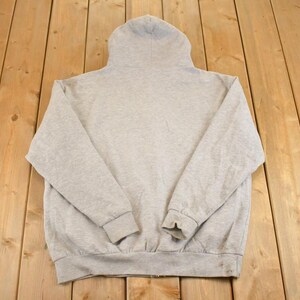 Op de afbeelding: Een lichtgrijze hoodie met een volledige ritssluiting. De hoodie is gemaakt van een zacht, comfortabel materiaal. De capuchon is omhoog en de mouwen zijn lang met geribde manchetten. De hoodie ligt plat op een houten oppervlak.