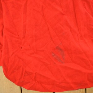 May include: A bright red long-sleeved shirt with a buttoned cuff. The fabric has some wrinkles and minor discoloration. The shirt's bottom hem is curved.