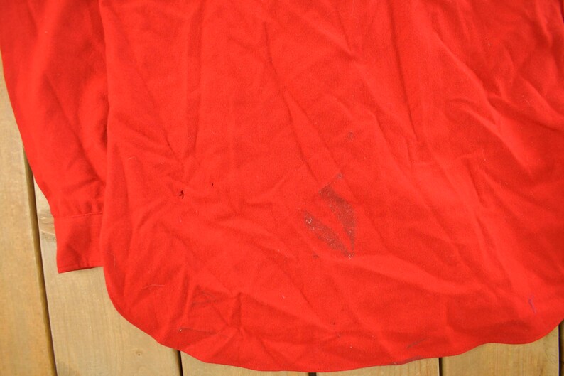 May include: A bright red long-sleeved shirt with a buttoned cuff. The fabric has some wrinkles and minor discoloration. The shirt's bottom hem is curved.