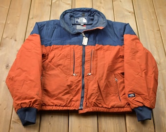 May include: A blue and orange vintage The North Face jacket with a zipper closure and a logo on the left chest.