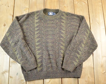 May include: A brown and green patterned sweater with a crew neck. The sweater features a geometric design in shades of green and brown. The ribbed cuffs and hem provide a snug fit. The sweater is made of a soft, knitted material.