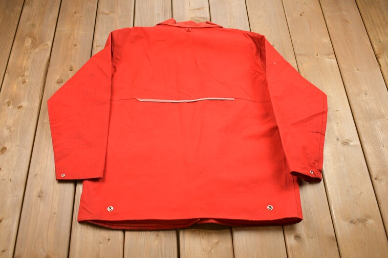 May include: A red long-sleeved jacket with a zipper on the back and silver buttons.
