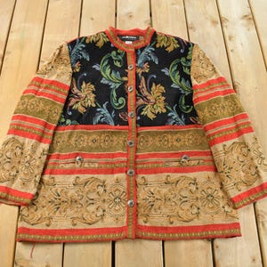 May include: A vintage jacket with a floral and striped pattern. The jacket features a black floral centre panel, button closure, and a mix of red, tan, and green stripes and patterns. The jacket is laid flat on a wooden surface.