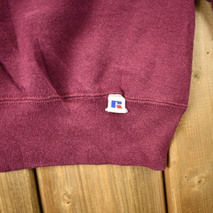 May include: Burgundy sweatshirt with a small blue and white "R" logo tag sewn on the bottom right side.