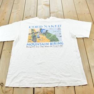 Könnte beinhalten: Ein weißes kurzärmeliges T-Shirt mit einem Grafikdruck auf der Rückseite. Das Motiv zeigt ein Mountainbike auf einem Pfad mit dem Text COED NAKED MOUNTAIN BIKING und dem Schriftzug Hang On For The Ride Of Your Life in Blau und Schwarz.