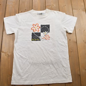 May include: White t-shirt with a black and white chequered design and orange and white flowers. The text "Love you like" is printed on the shirt.