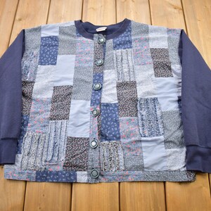 May include: A blue patchwork cardigan with a button-up front. The cardigan is made of different fabrics with floral patterns in shades of blue and pink.