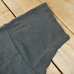 May include: Close-up of the dark gray fabric of a t-shirt. The fabric has a smooth texture and is folded over on itself.