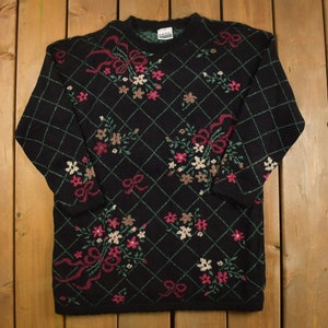 Peut inclure: Pull-over noir avec un motif floral et des nœuds sur un fond vert foncé. Le pull a un motif en forme de diamant.