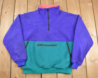 May include: A purple, teal and pink fleece pullover with a zipped pocket on the front.