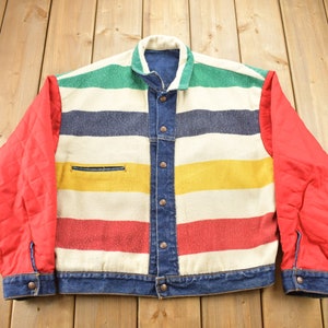 May include: A blue denim jacket with a striped pattern in red, yellow, green, and blue. The sleeves are red and the jacket has a button closure.