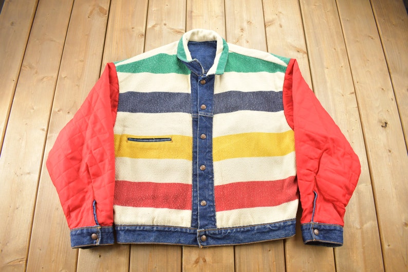 May include: A blue denim jacket with a striped pattern in red, yellow, green, and blue. The sleeves are red and the jacket has a button closure.