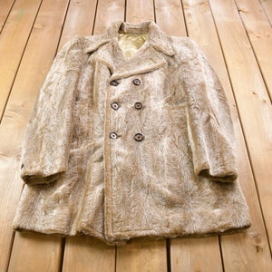 Peut inclure: Un manteau en fausse fourrure marron avec une fermeture à double boutonnage et quatre boutons. Le manteau est posé à plat sur une surface en bois.