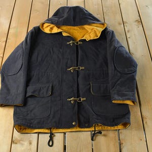 May include: A navy blue hooded duffle coat with a yellow interior. The coat features toggle closures, two front pockets, and elbow patches. The hood and cuffs are lined with yellow fabric.