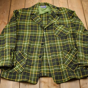 Può includere: Una giacca a quadri verde, gialla e nera con chiusura a bottoni e due grandi tasche.