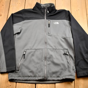 May include: A gray and black fleece jacket with a zipper closure and the text "The North Face" on the chest.