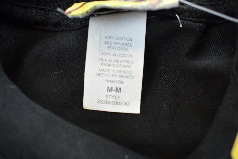 May include: A close-up of a black garment with a white label. The label states the item is 100% cotton, with care instructions. It also indicates the item was made in Mexico, size M-M, and style code SS2B50002DO.