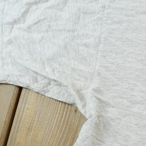 Op de afbeelding: Een lichtgrijs gem&ecirc;leerd t-shirt met een korte mouw en een zichtbare naad onder de arm. De stof heeft een gespikkelde textuur en toont een casual gebreide constructie met een standaard zoom en een eenvoudig, effen ontwerp.