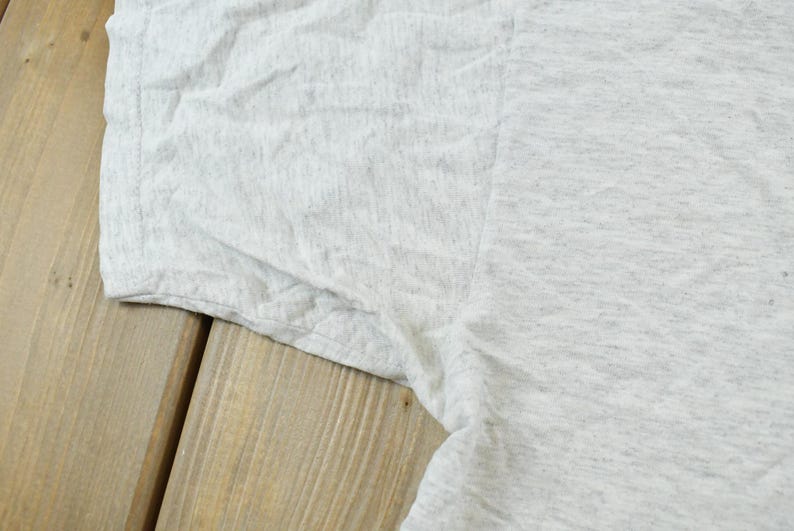 Op de afbeelding: Een lichtgrijs gem&ecirc;leerd t-shirt met een korte mouw en een zichtbare naad onder de arm. De stof heeft een gespikkelde textuur en toont een casual gebreide constructie met een standaard zoom en een eenvoudig, effen ontwerp.