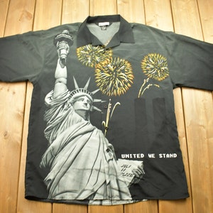 May include: A black short-sleeved button-up shirt with a print of the Statue of Liberty, fireworks, and the words "United We Stand" and "July 11, 2001".