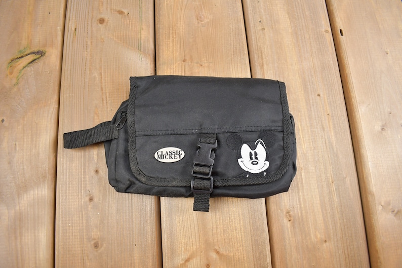 Op de afbeelding: Zwarte reistas met rits, een Mickey Mouse-gezicht en de tekst "Classic Mickey" aan de voorkant.